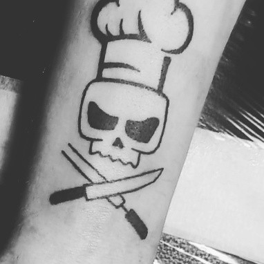 ein Tattoo, welches ein Kochmotiv im Piratenstil darstellt