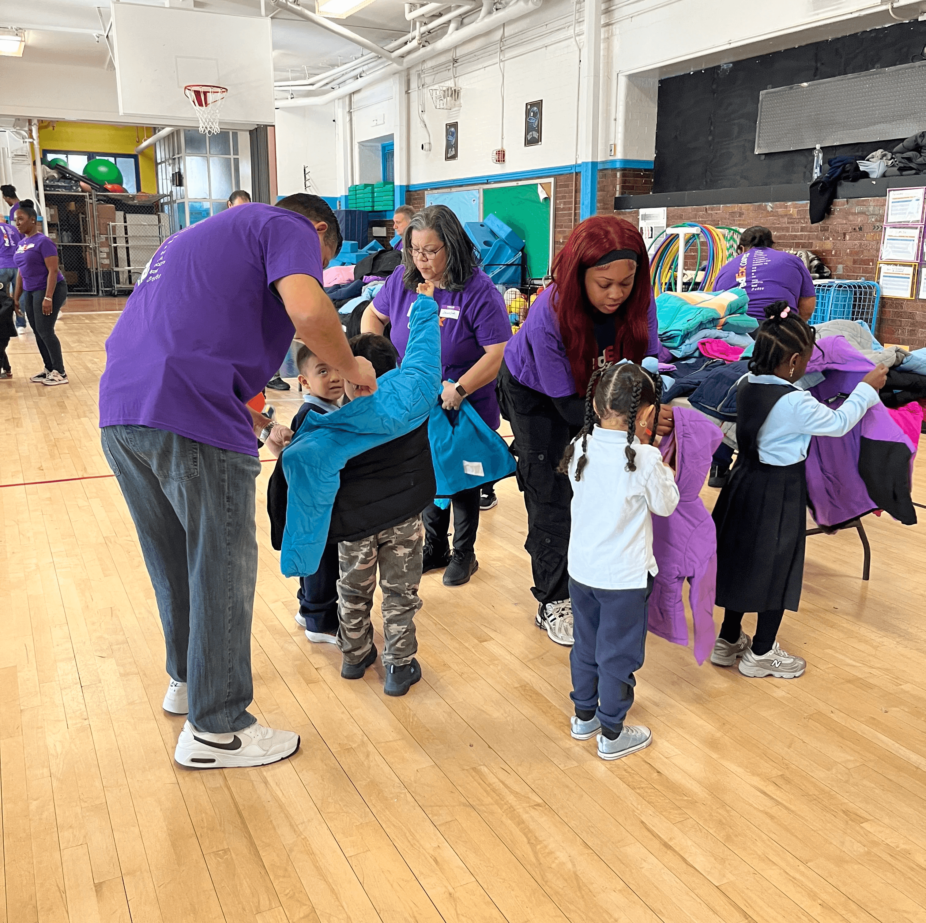 FedEx volunteers help young students try on coats at a coat drive.