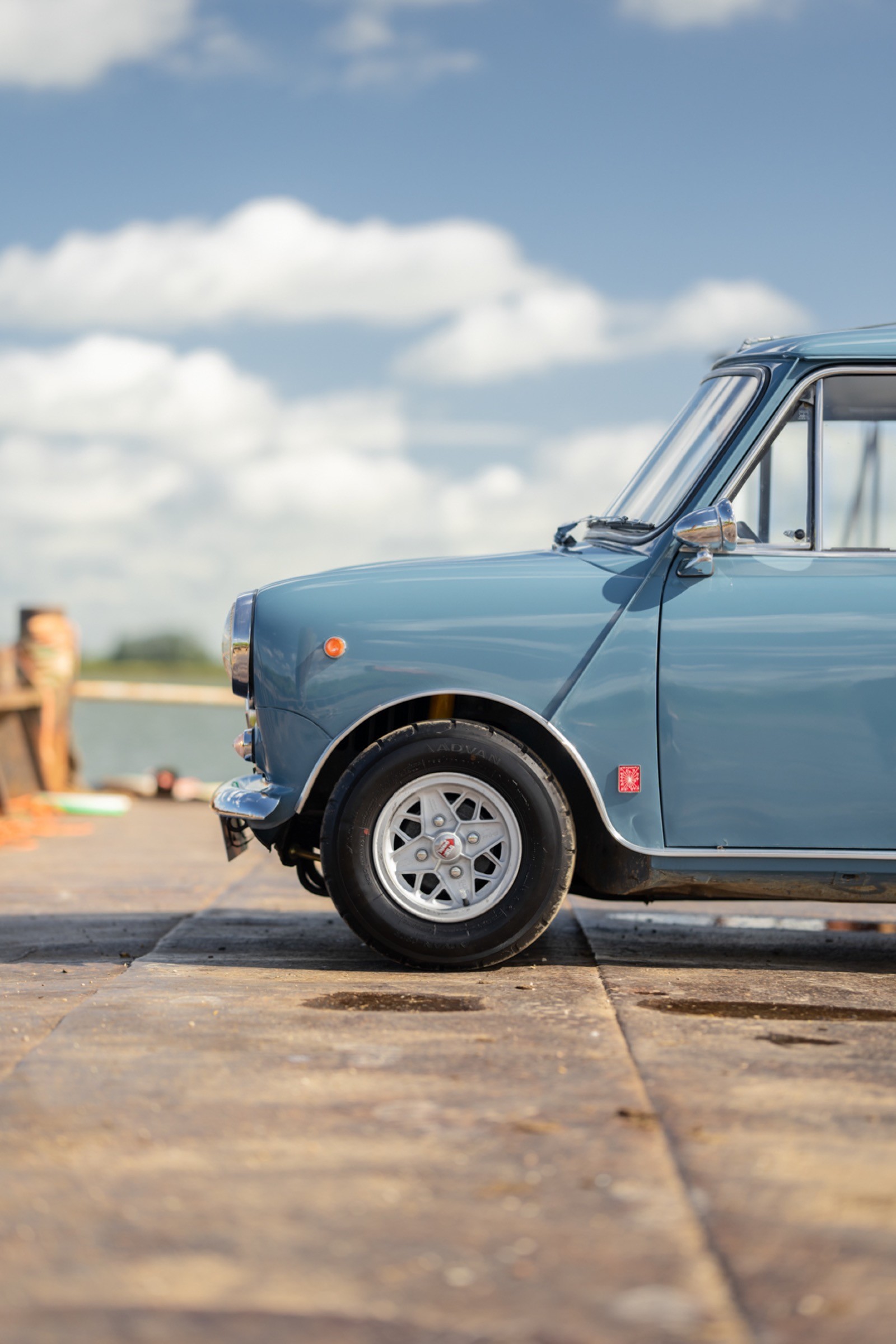 A vintage blue car parked on a sunny street, with a clear sky and distant landscape visible.