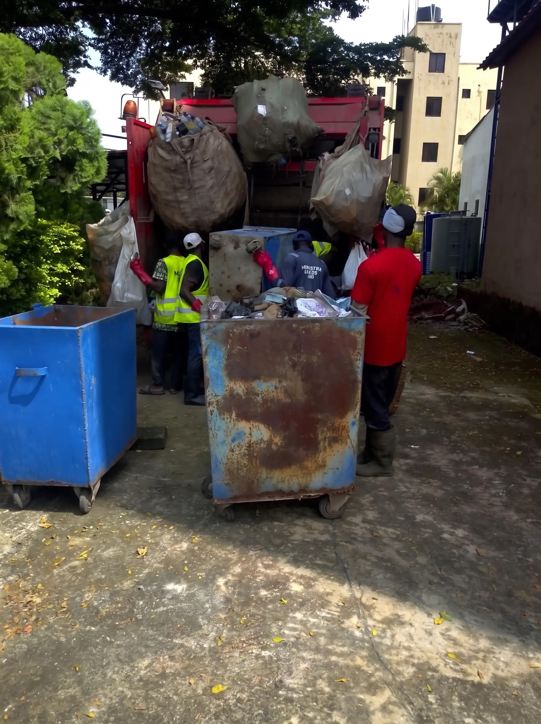 Waste collection crew loading bagged rubbish and emptying wheeled bins into a refuse truck.