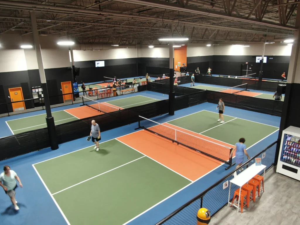 Overhead view of completed indoor pickleball facility with multiple courts in use, featuring green and orange court surfaces