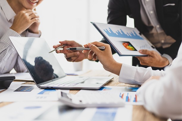 A talent recruiter with a soft smile working on her laptop in the office. The angle is on her face so we can't see what's is on the screen. She is wearing a blazer 