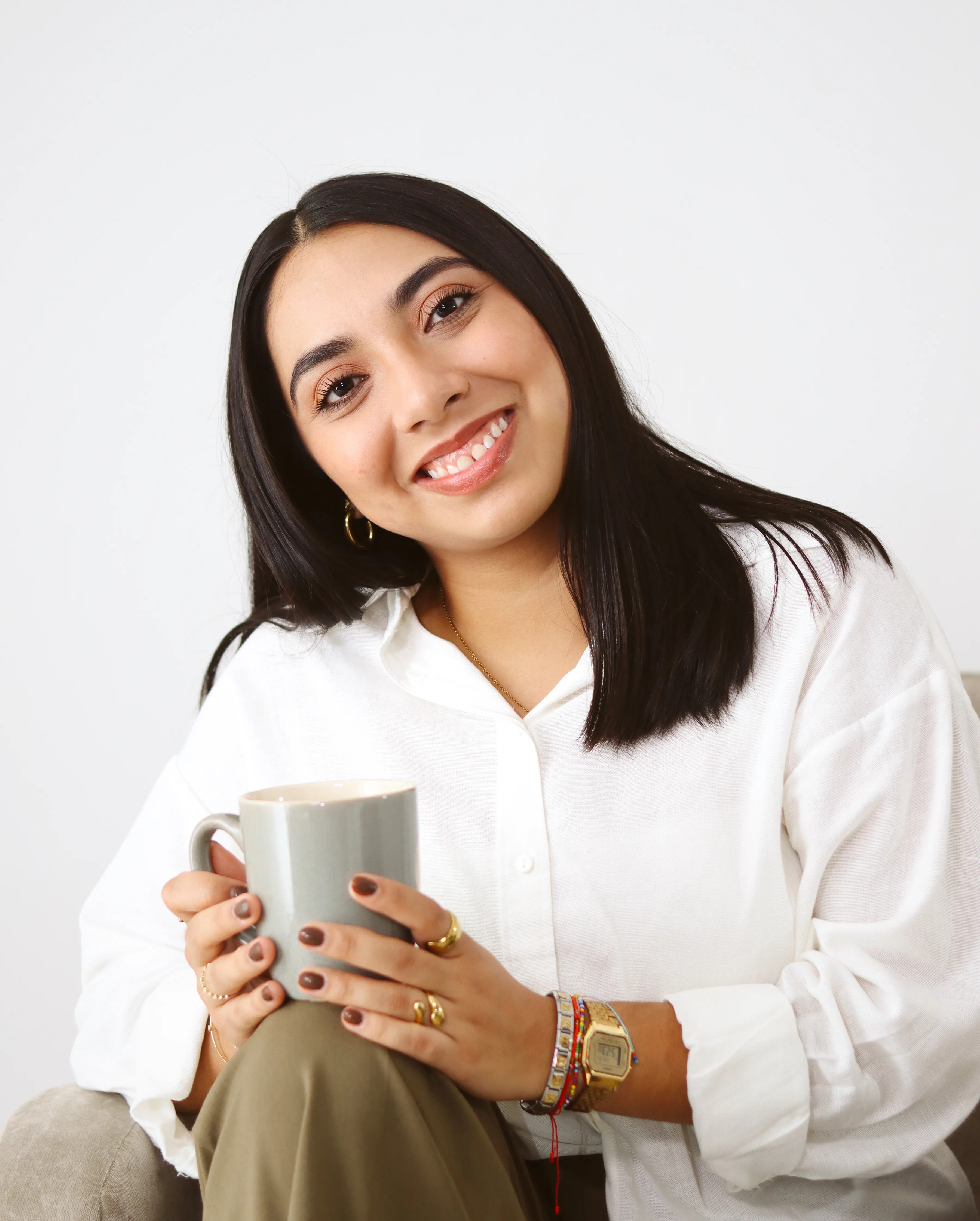 Mujer sonriendo mientras sostiene una taza blanca.