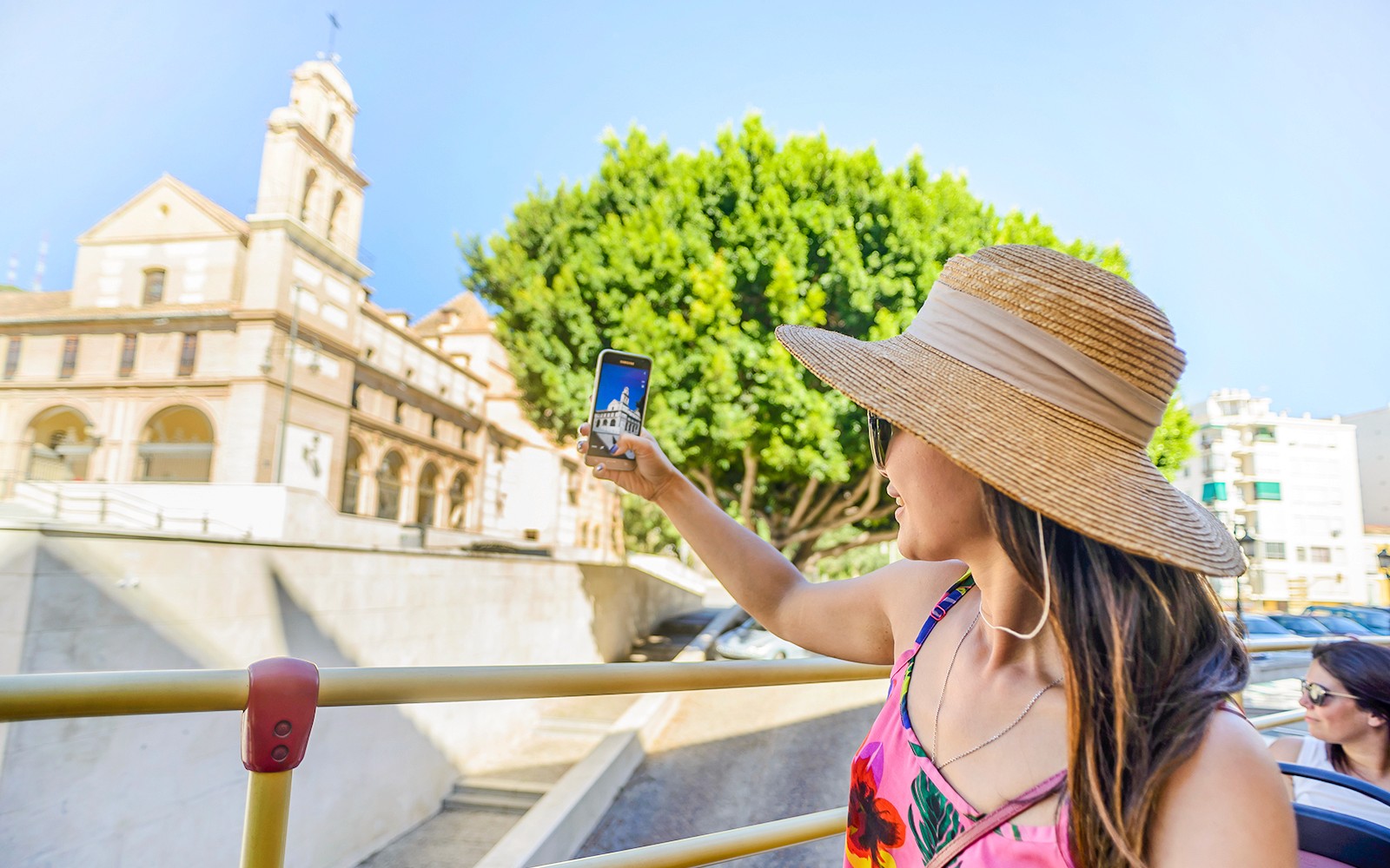 Woman taking photo from open-top bus on Malaga city tour.