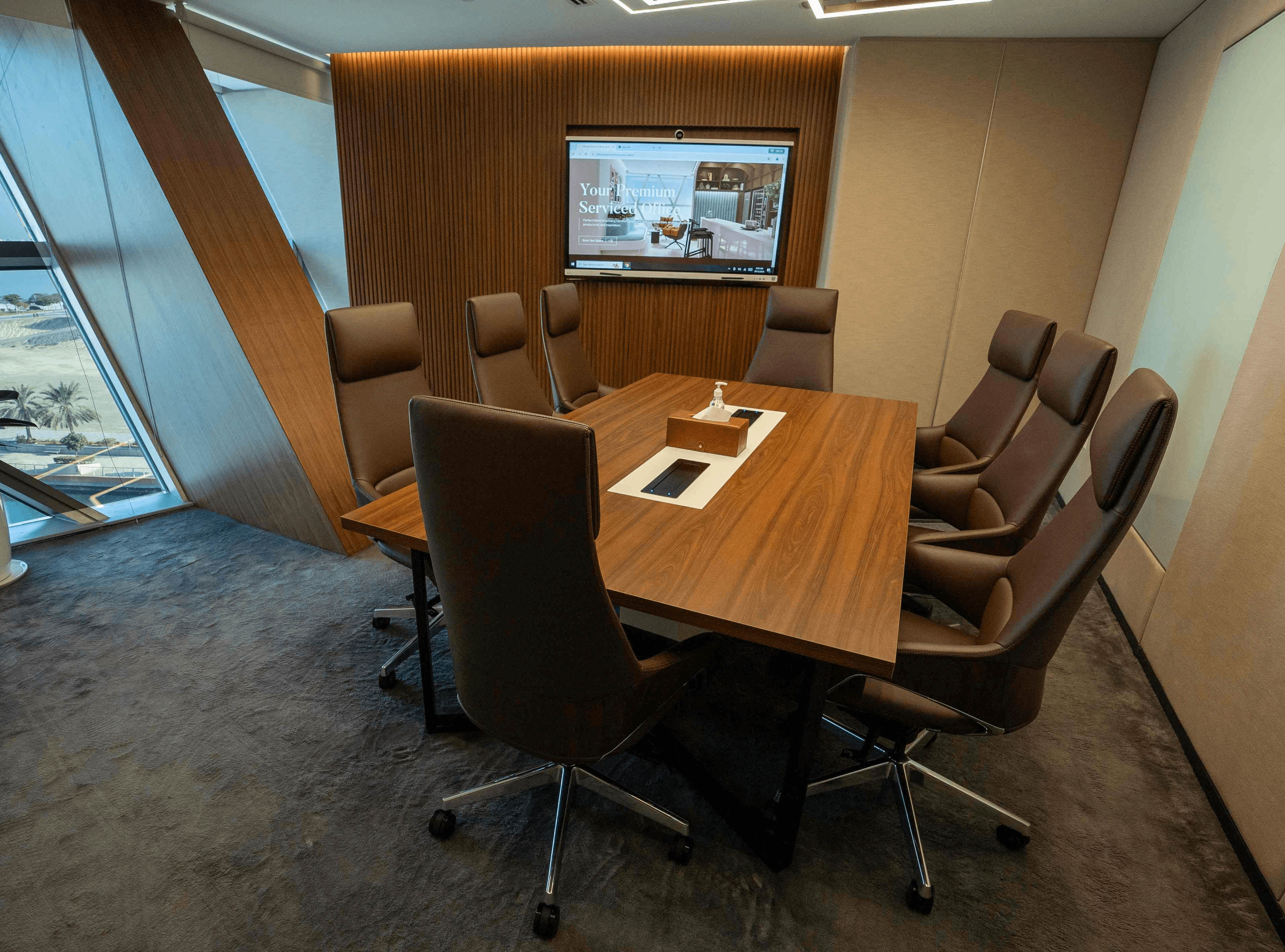 Premium meeting room in Abu Dhabi featuring a wood-paneled wall, high-definition screen, and an 8-seater conference table.