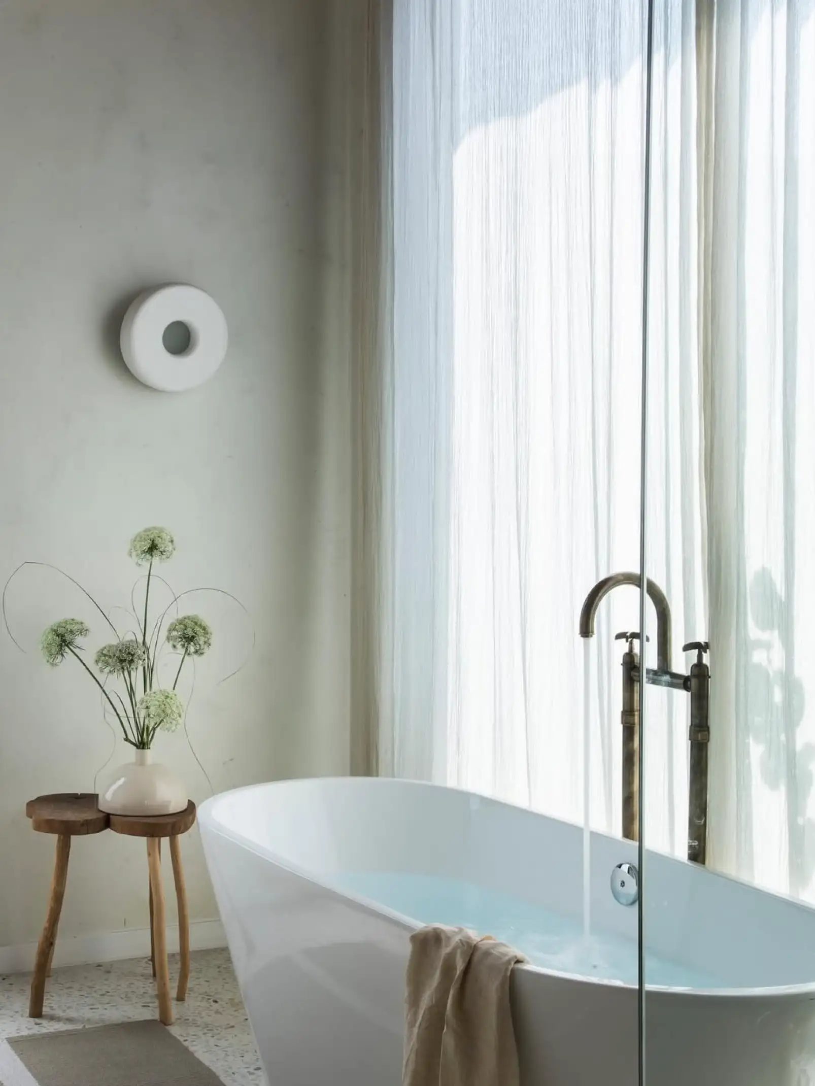 Baño luminoso con bañera exenta y flores blancas para diseñadores que priorizan bienestar y estética serena.