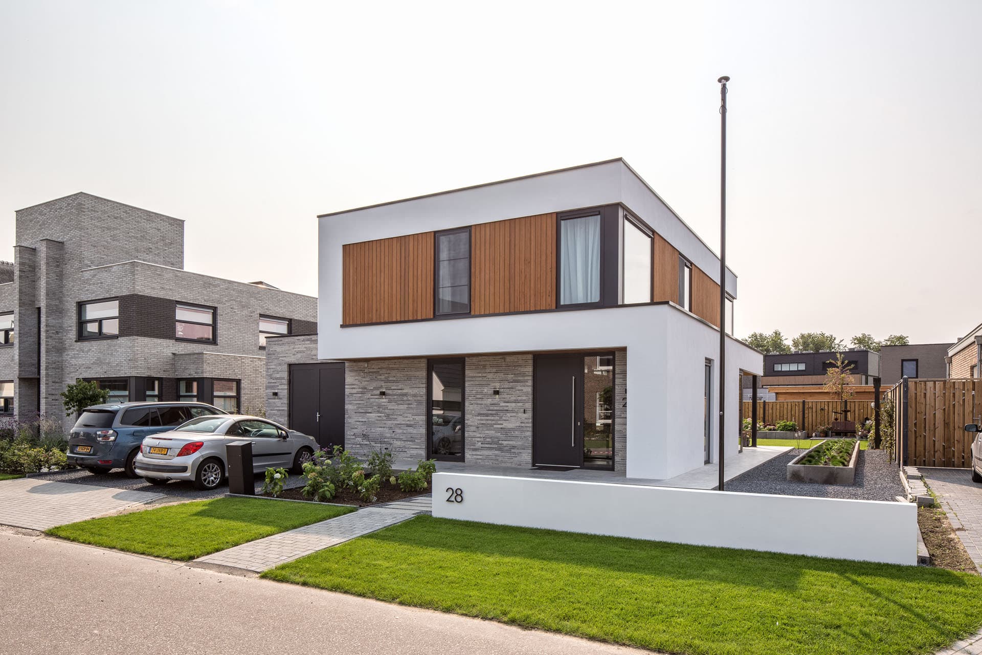 Voorzijde van moderne villa met witte gevel, houten verdieping en lichte bakstenen plint