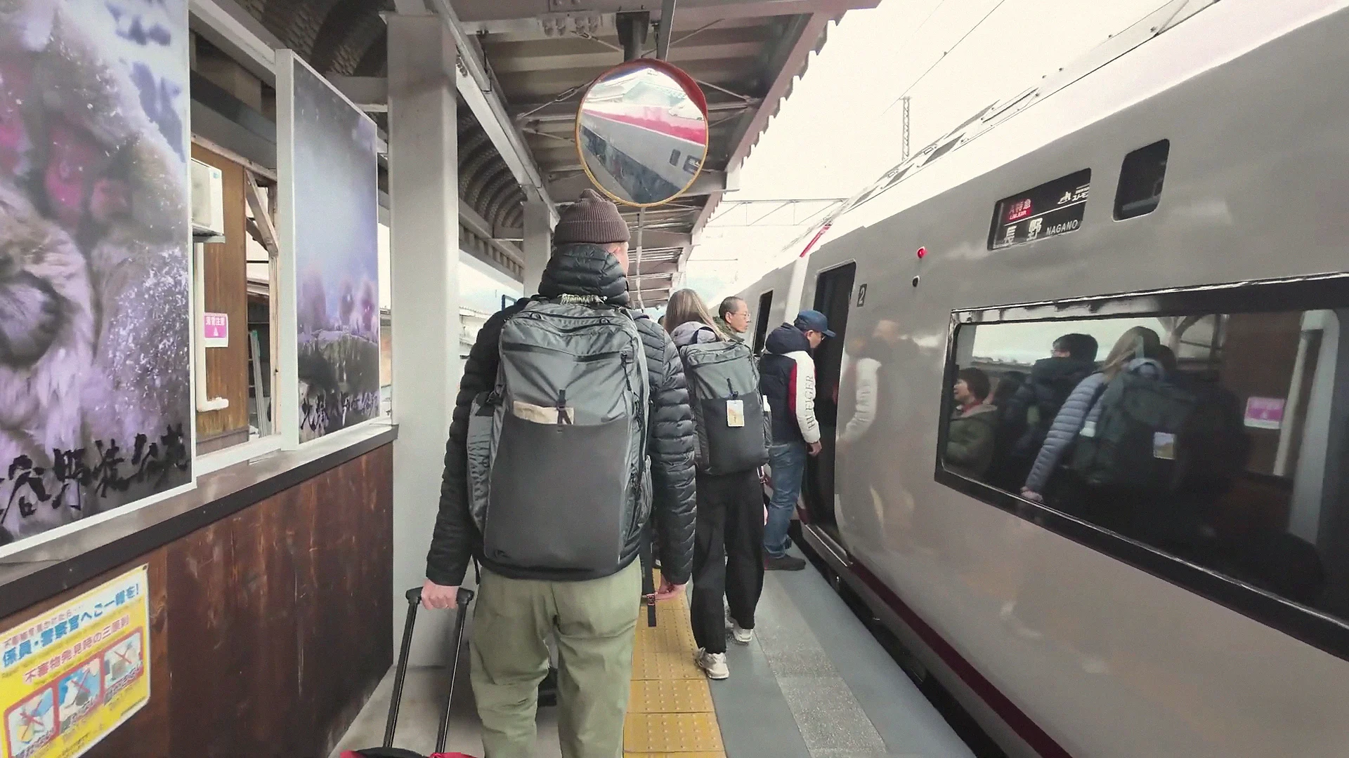 Travellers board the Nagaden 'Snow Monkey' limited express (bound for Nagano) at Yudanaka Station, snow-monkey photos on the platform wall.