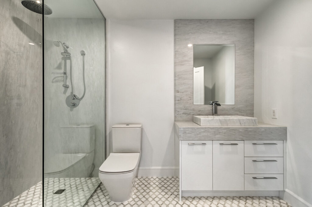 Modern condo bathroom remodel featuring a frameless glass shower, grey marble vanity with vessel sink, and geometric floor tiles, highlighting B&Y Reno Corp’s clean and minimalist design approach