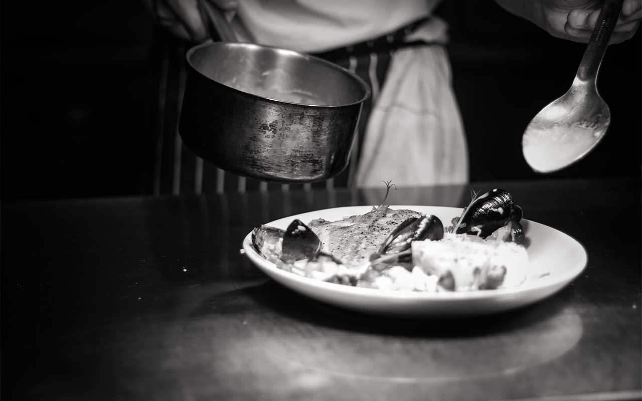 A black and white photo of a chef plating a dish of fish and seafood