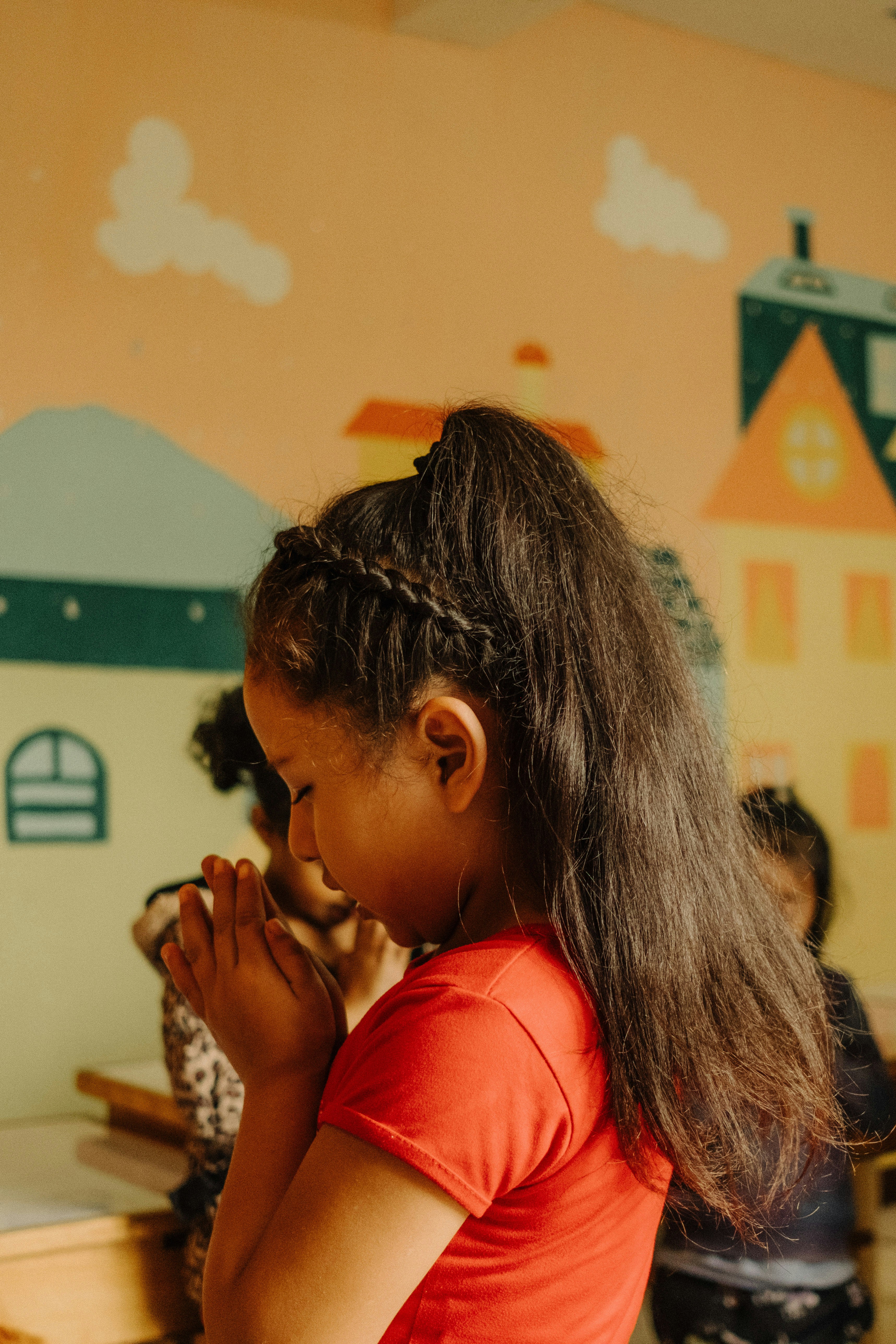 a young girl sitting at a desk with her hands clasped