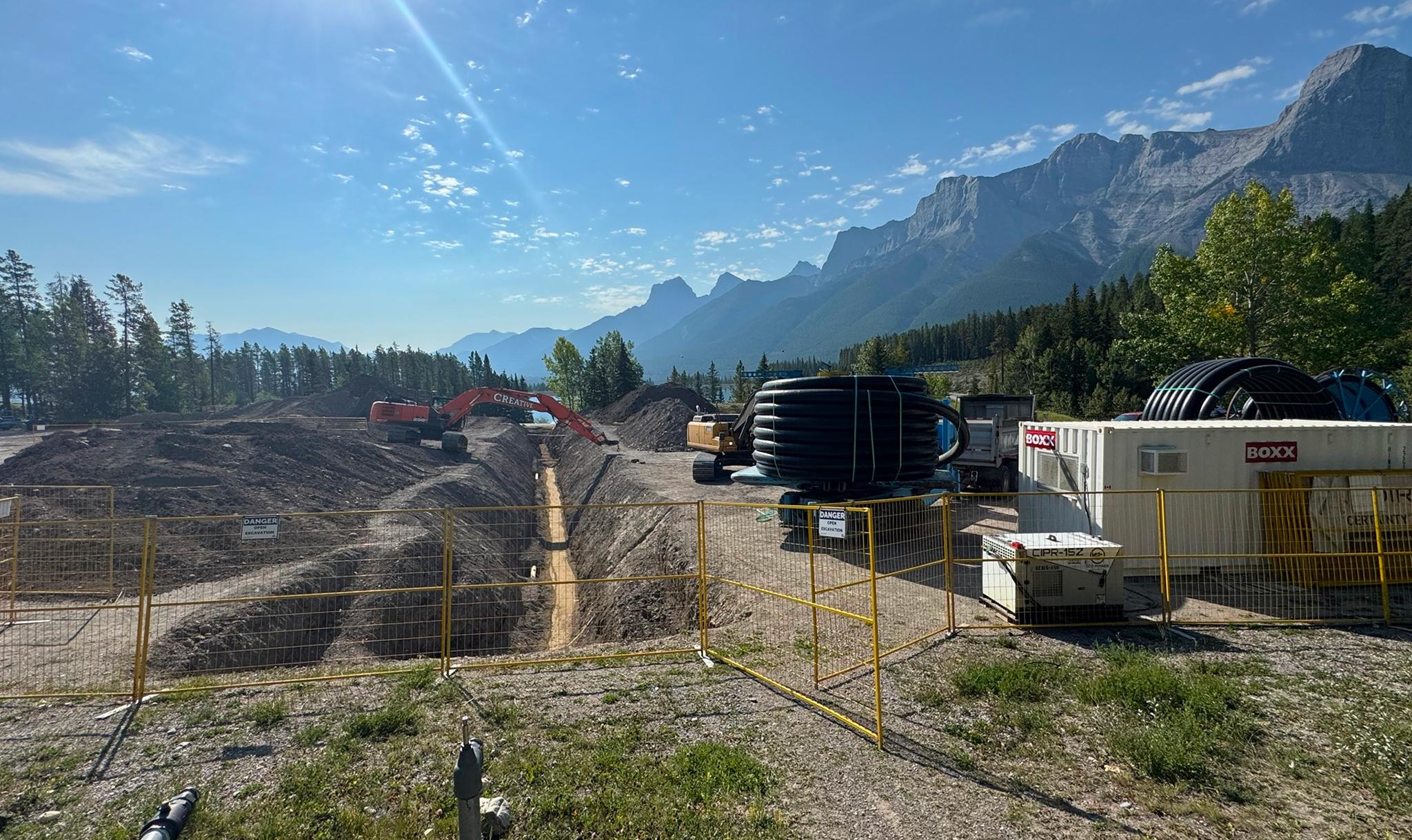 Pipeline construction for Canmore Nordic Centre snowmaking system with excavation and equipment in Rocky Mountains