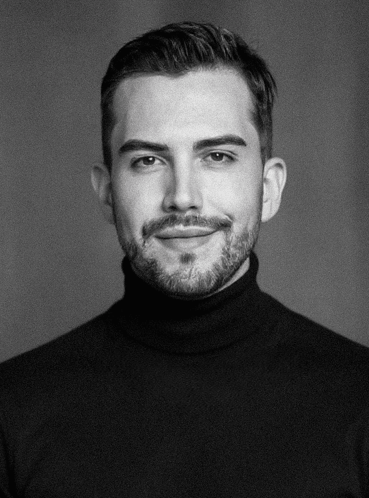 A thoughtful young person with dark hair gazes to the side, captured in soft black and white lighting.