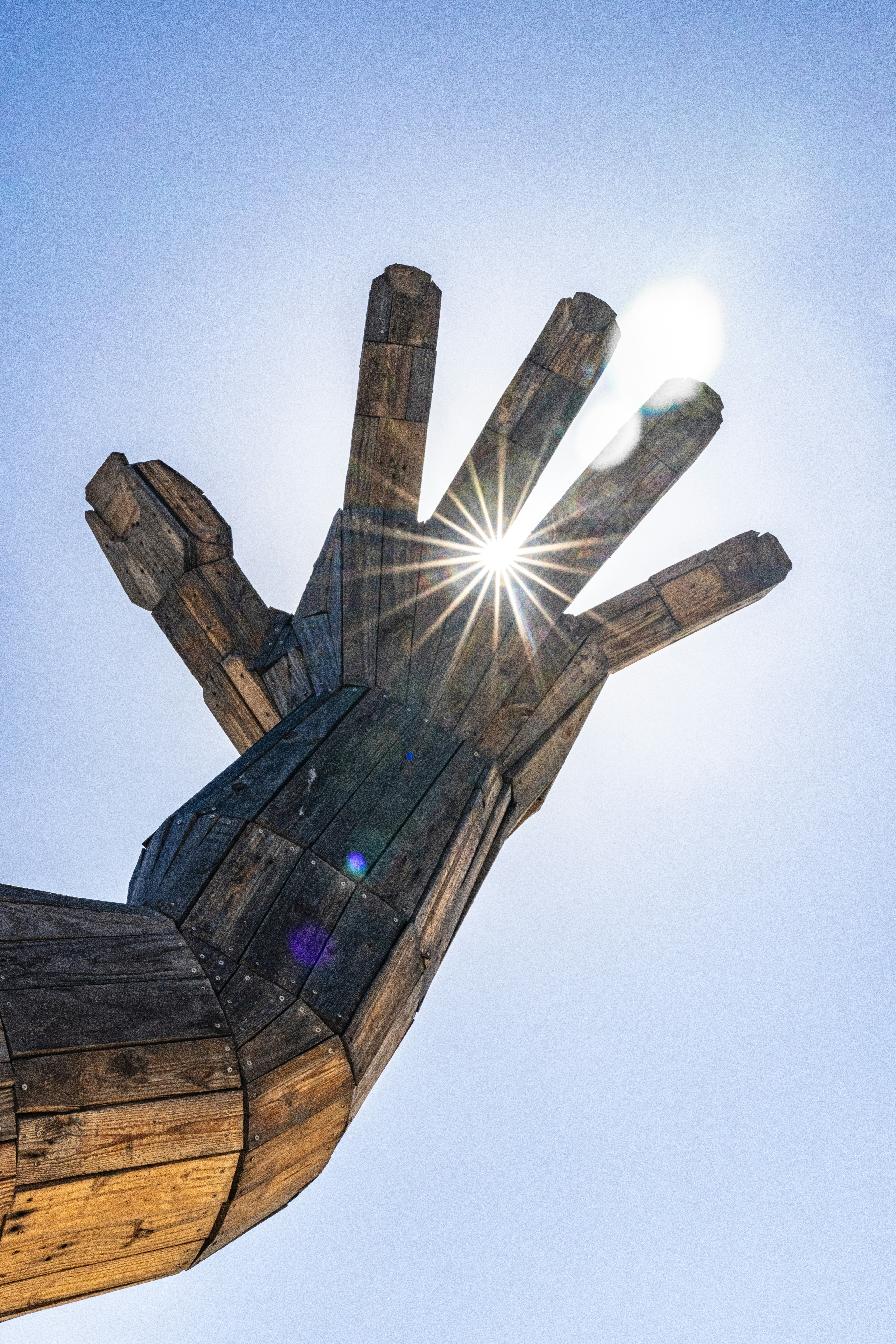 Giant wooden hand sculpture with sun shining through fingers.