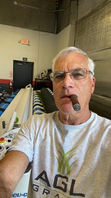 Jerry Lawrence, owner of AGL Grass North, poses in front of the artificial grass-cutting machine at his Rocklin, CA., warehouse and showroom.