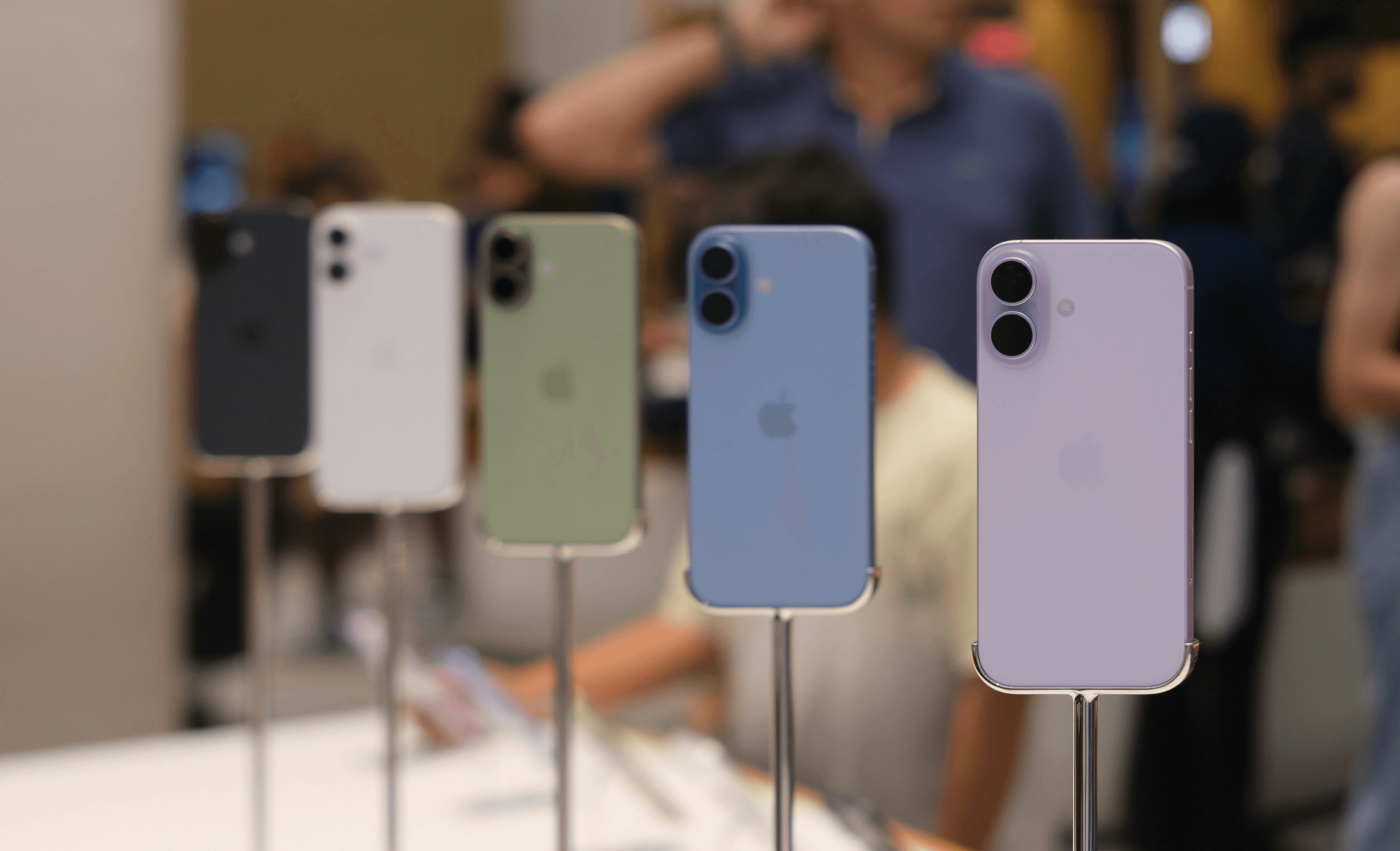 Five iphones displayed in various colors on stands.
