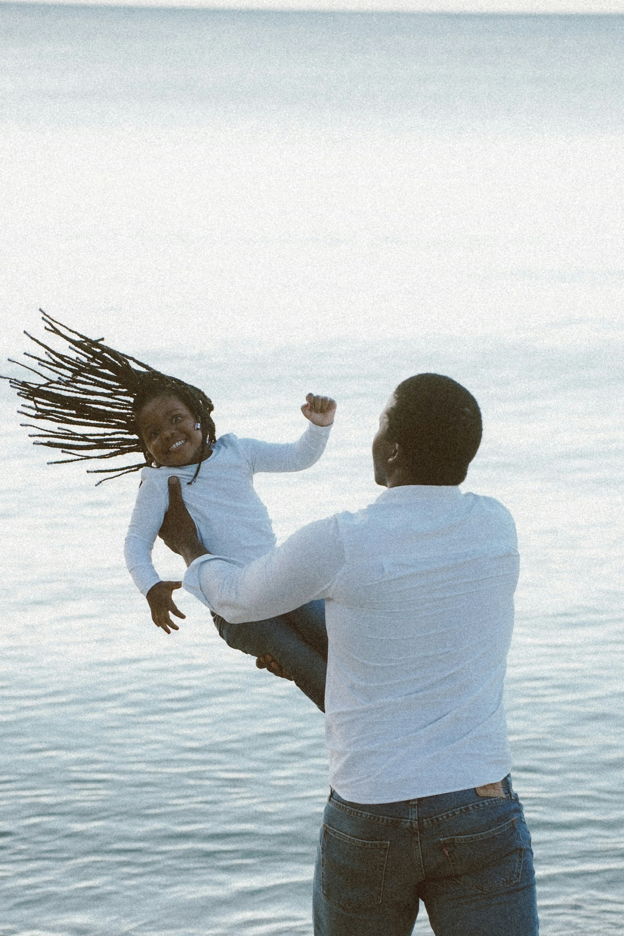 Father swinging happy daughter by the water