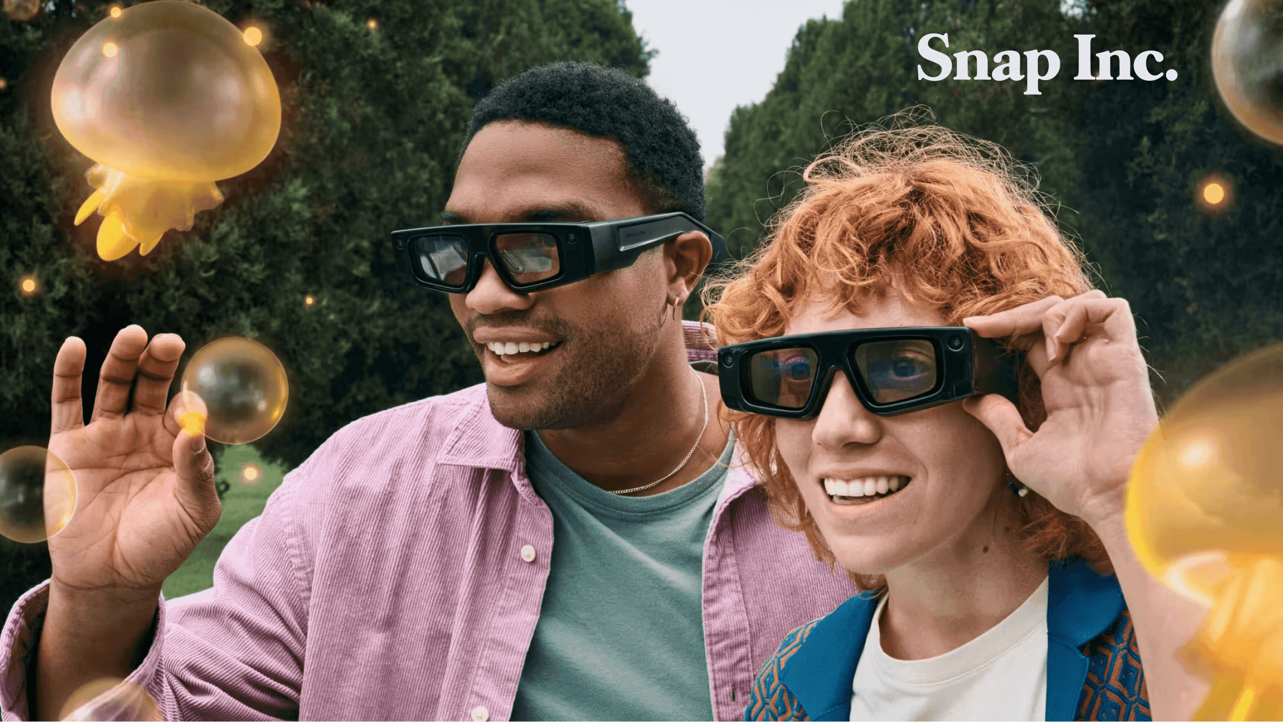 Two users wearing Snap Inc. AR Spectacles experiencing an outdoor augmented reality overlay featuring holographic jellyfish, demonstrating the device's lightweight form factor and shared AR capabilities.