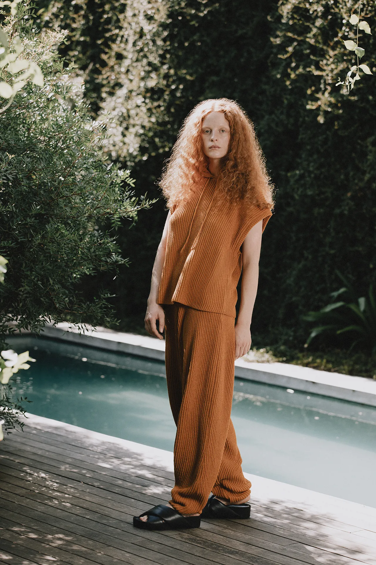 Annapurna SS26 collection rust-orange ribbed knit set featuring a sleeveless hooded top and wide-leg trousers.