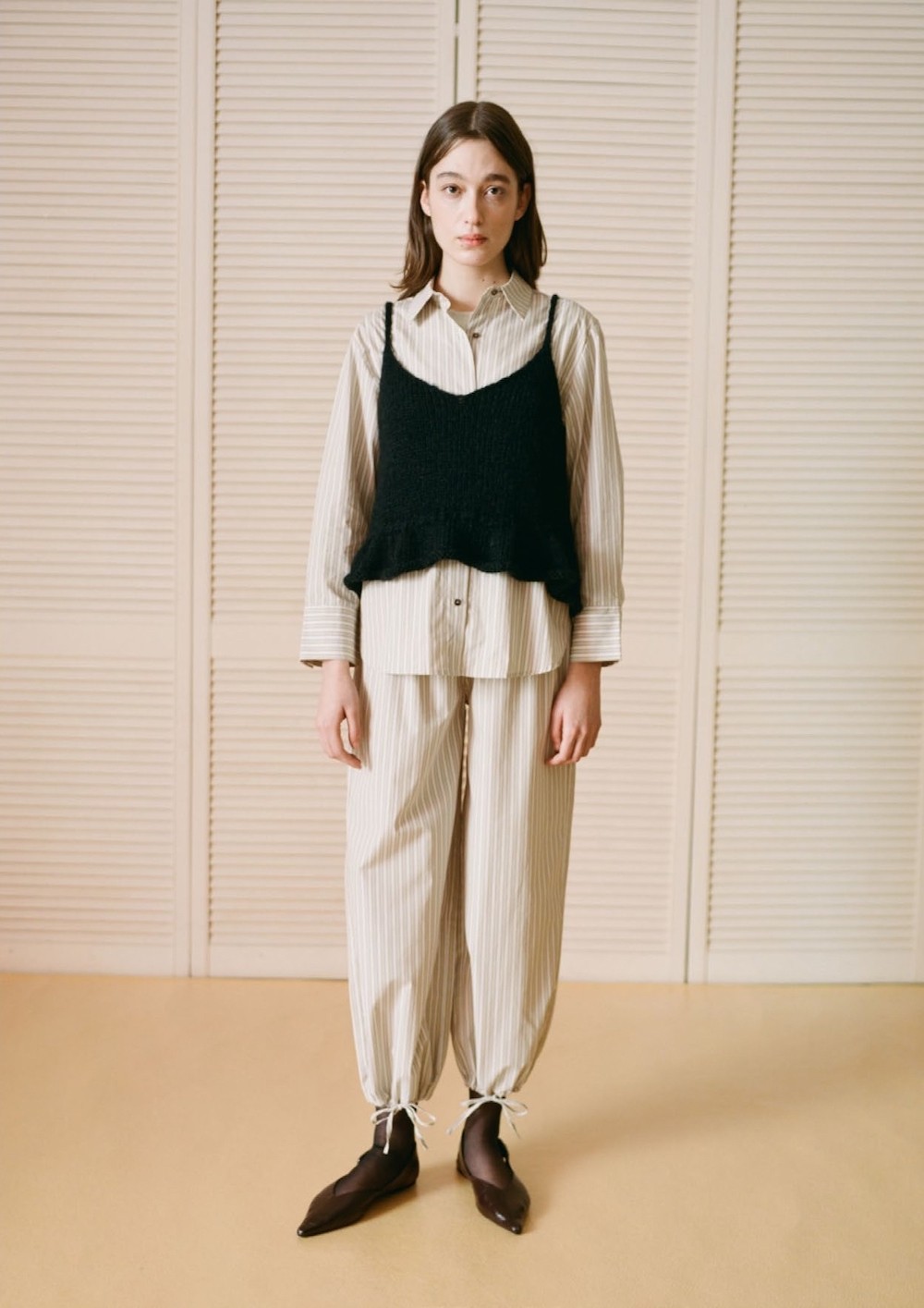 Une femme porte un esnemble façon pyjama blanc cassé ample et un tablier en maille noire