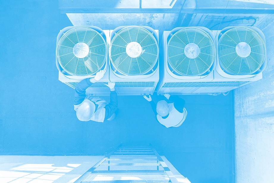 A blue-toned aerial view of two workers servicing multiple air conditioning units on a rooftop, with the units lined up in a row.