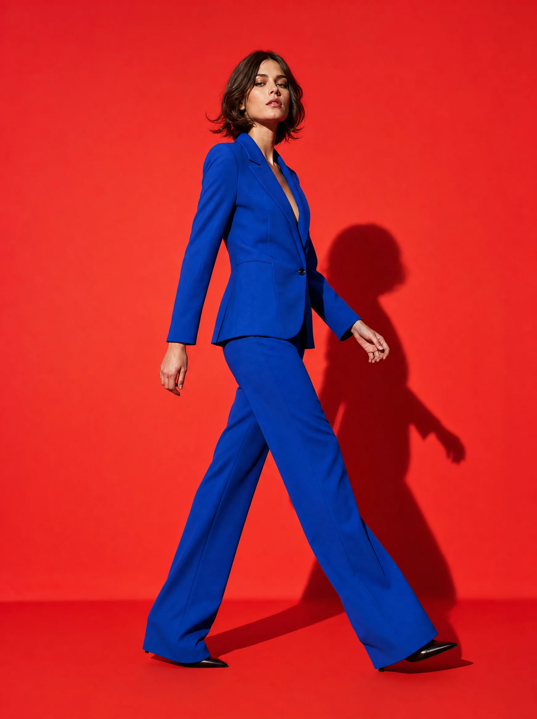 Model in a cobalt suit walking across a red paper backdrop