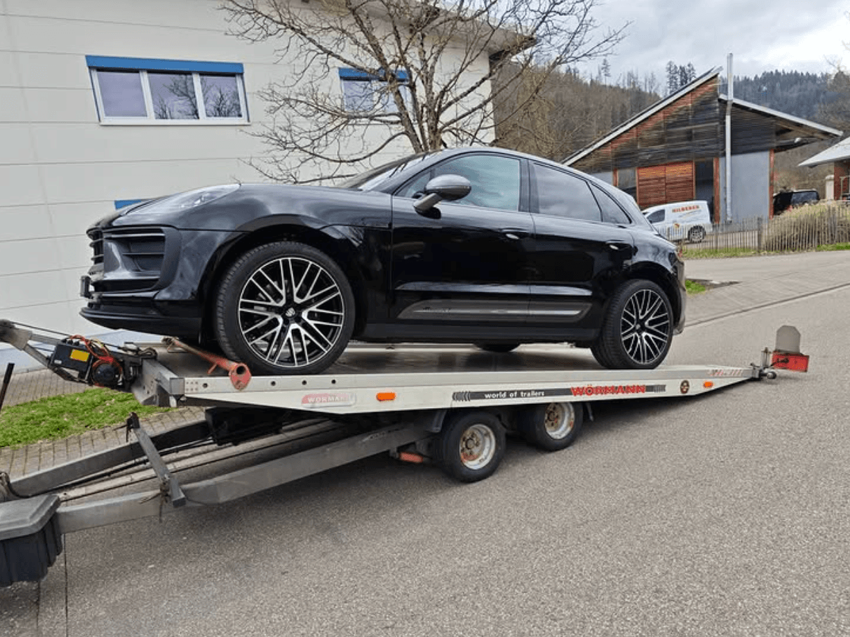 Schwarzer Porsche Macan auf einem Autotransport-Anhänger