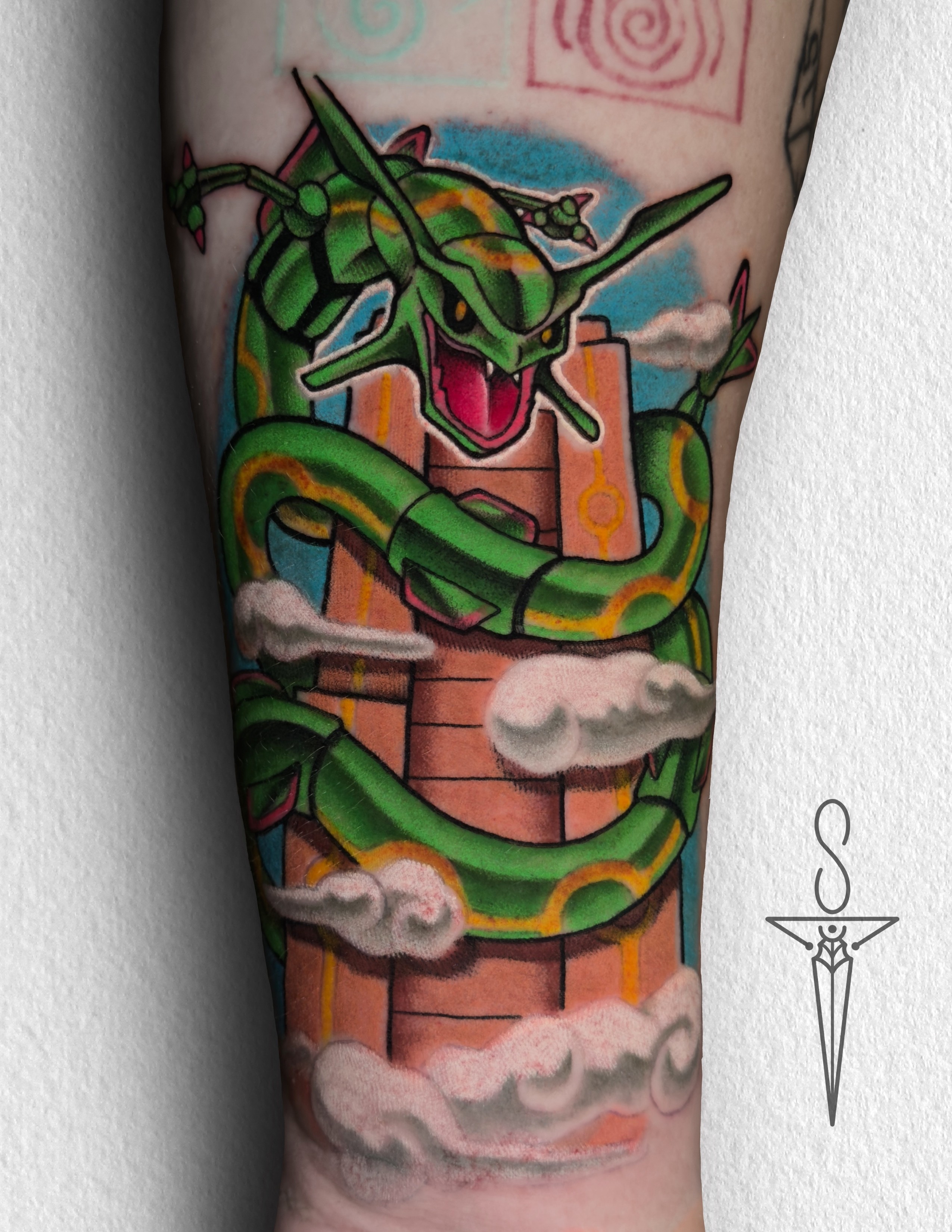 A vibrant tattoo of a chainsaw-like creature on a person's forearm. The tattoo is detailed with shades of orange, black, teal, and red.