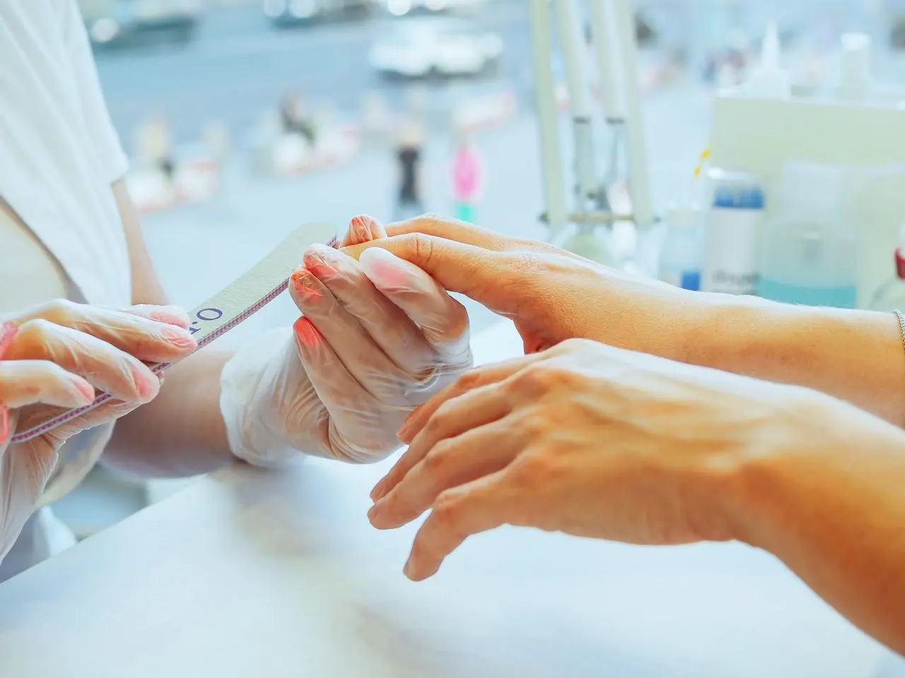 Profissional de manicure utilizando uma lixa para modelar as unhas de uma cliente durante atendimento em um salão de beleza.