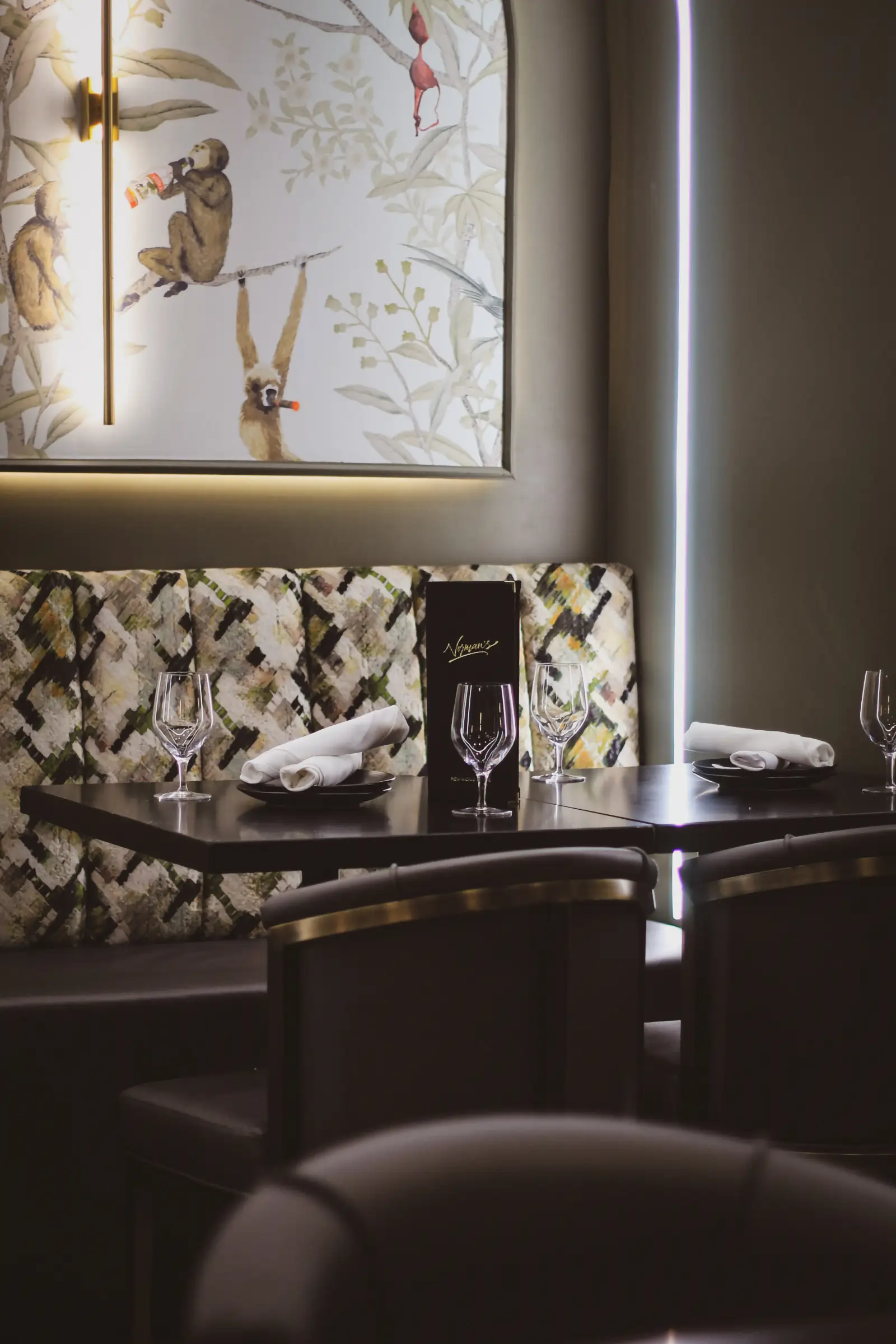 A restaurant booth with a dark table set for two. The wall behind features artwork of monkeys.