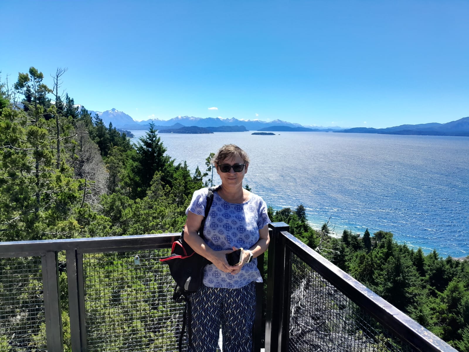 Mujer sentada sobre un tronco frente a una cascada doble en un bosque frondoso de Argentina.