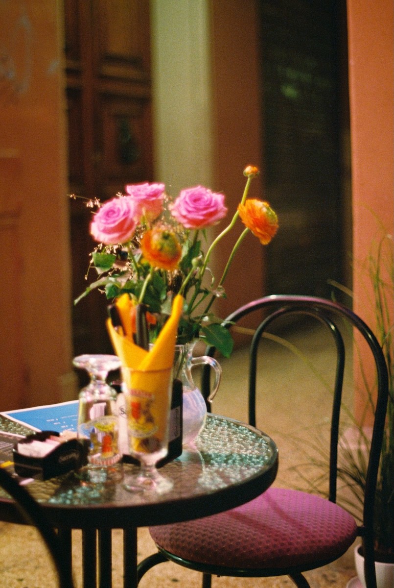 Empty outdoor table in Bologna street with a vase of pink flowers.