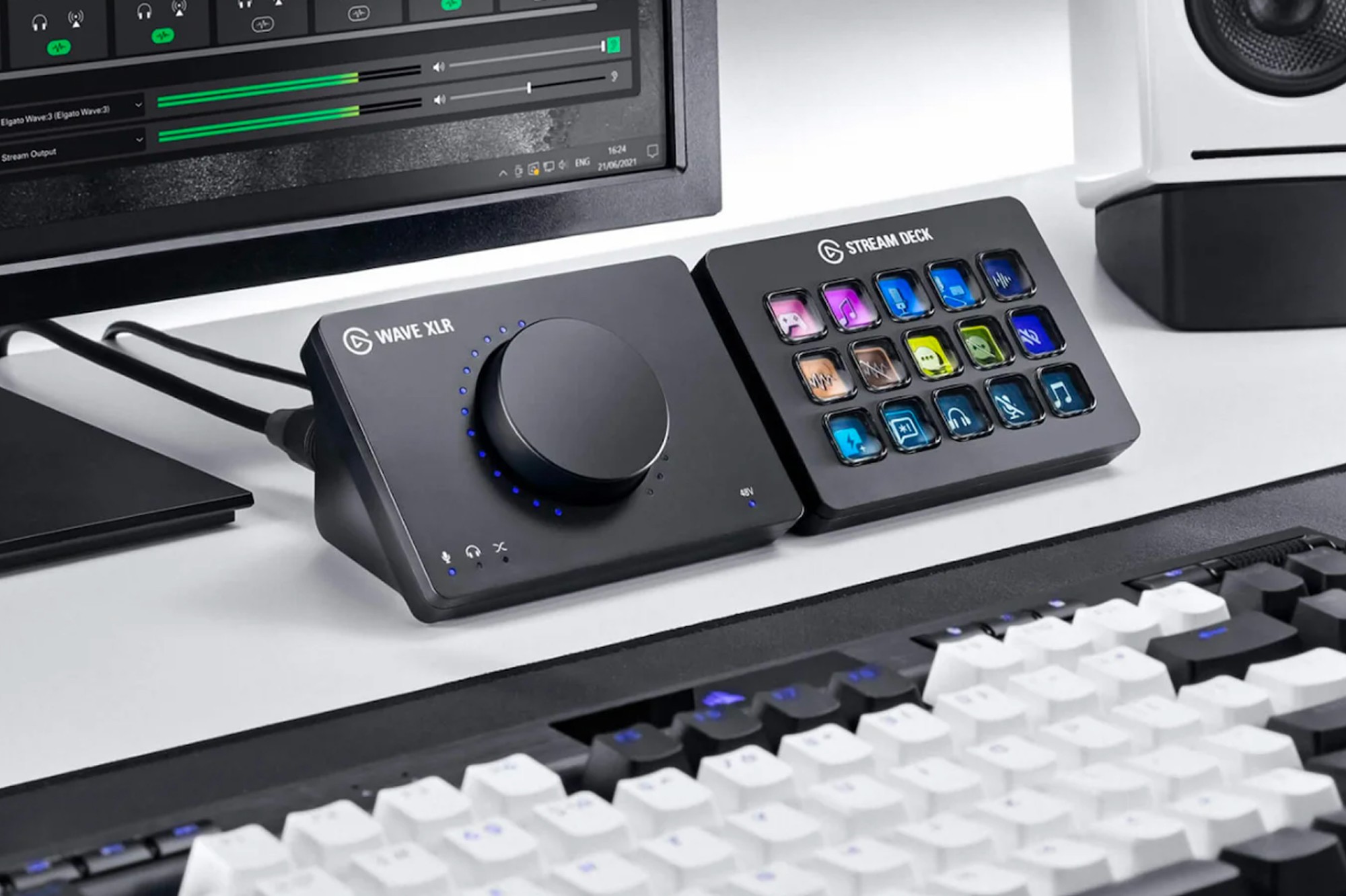 Image of the Elgato Wave XLR as part of a desk setup. It is next to a stream deck. A keyboard is in the foreground and a speaker and monitor are in the background