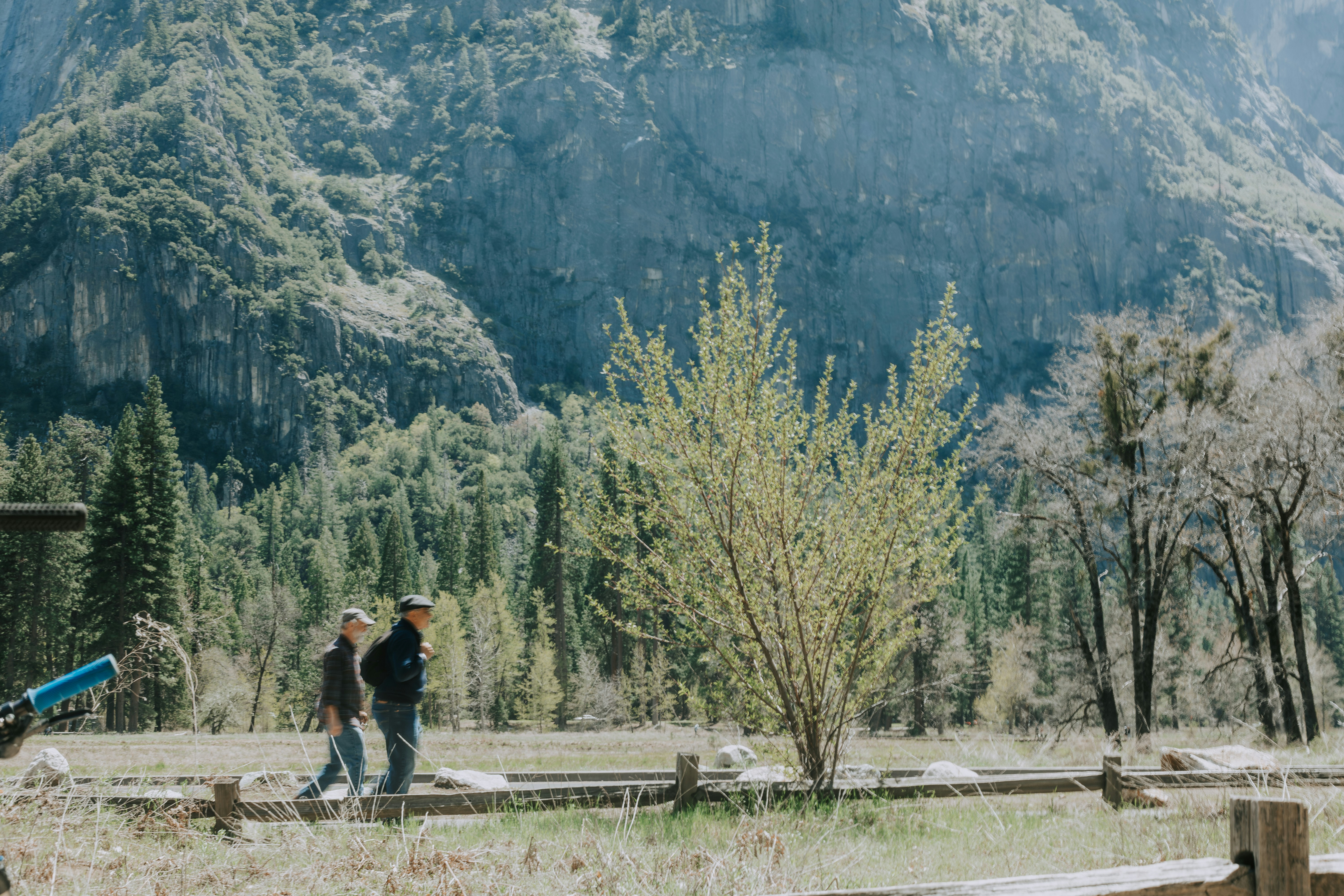 A winding road cuts through rocky terrain, surrounded by patches of green grass and illuminated by sunlight.