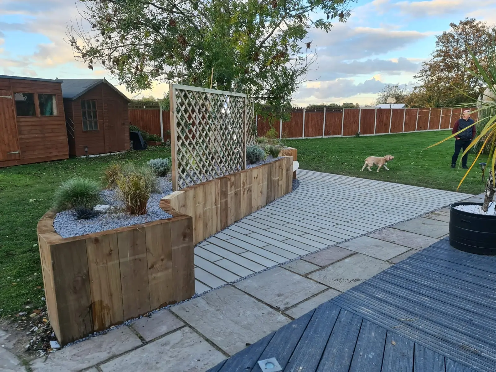 A garden view featuring a stone wall, potted plants, patio stones, and grass under a cloudy sky.