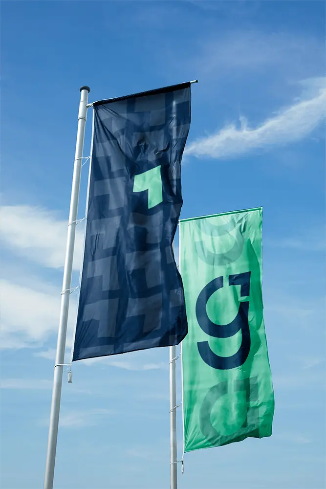 Gradure-branded flags in navy blue and green featuring the modern ‘G’ logo, waving against a clear blue sky
