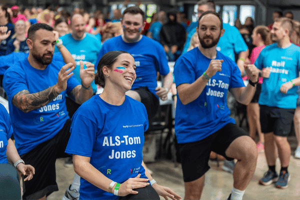 Outdoor team-building event with participants wearing matching blue shirts, taking part in inflatable obstacle courses and games, smiling and cheering, with the words 'ENTER A TEAM' in large bold white and green text across the image.