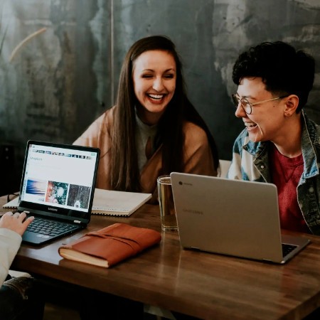 freinds sitting at a table with their laptops, lauging
