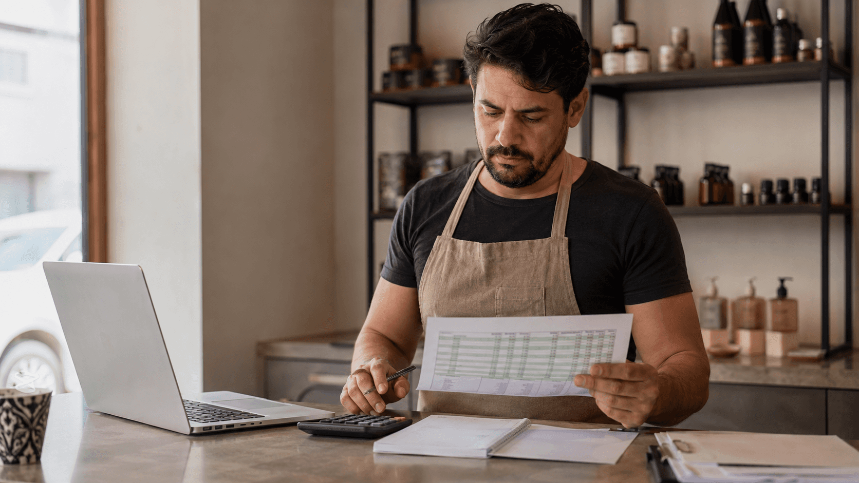 Dono de pequeno negócio analisando sozinho uma planilha no balcão da empresa