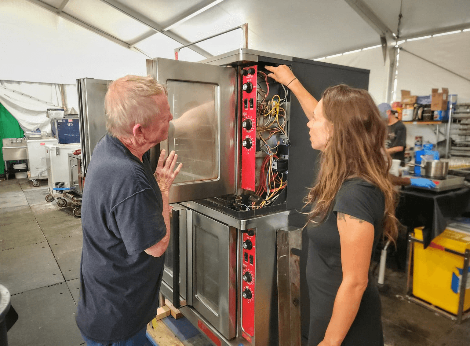 Two people are working together in a warehouse, unpacking boxes and organizing items in a workspace.