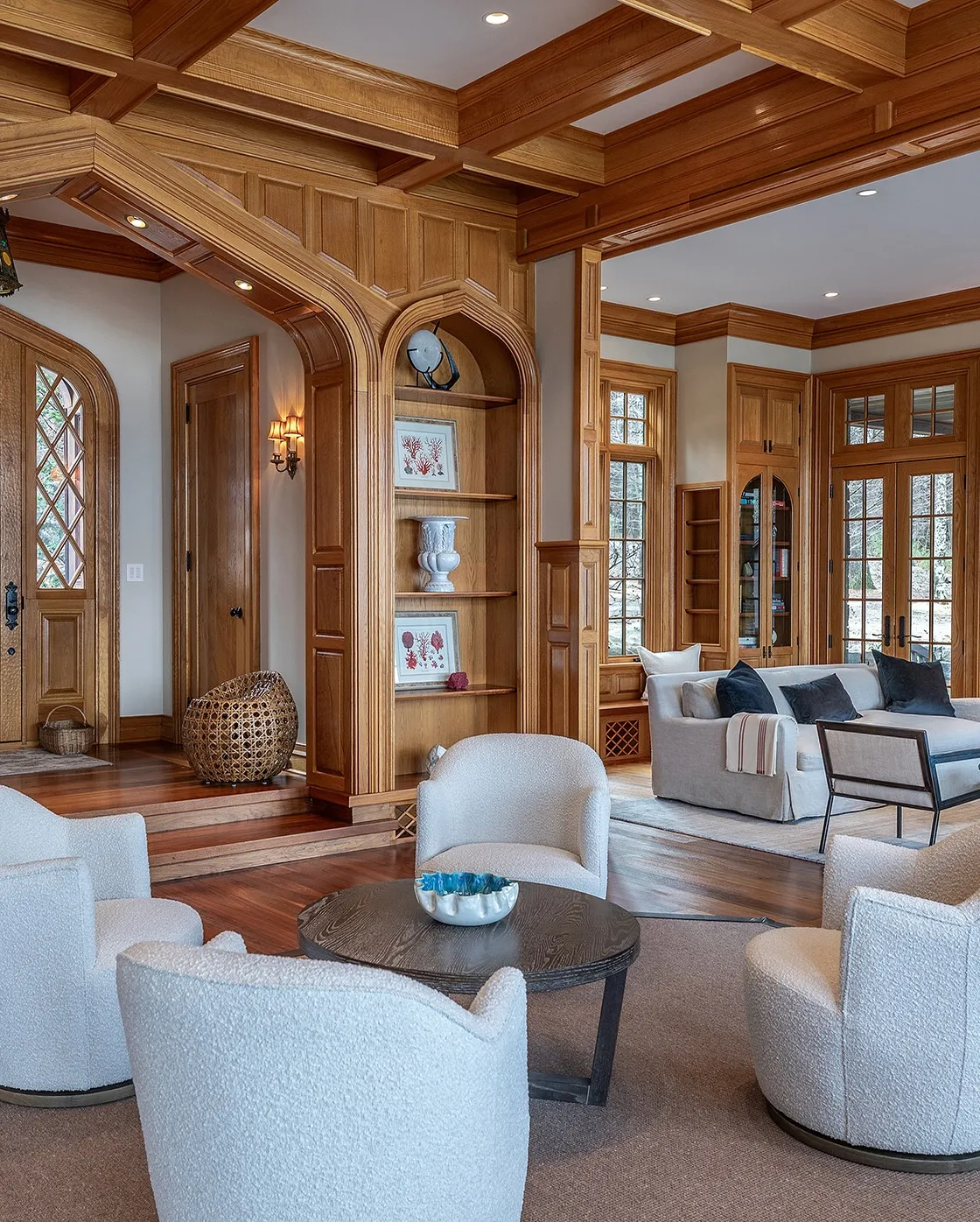 Cozy living room with dark wood paneling, arched windows, a mix of modern and classic furniture, and soft lighting.
