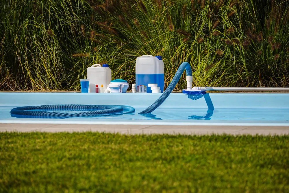 Poolside equipment including pumps, hoses, and chemical containers arranged on the grass.