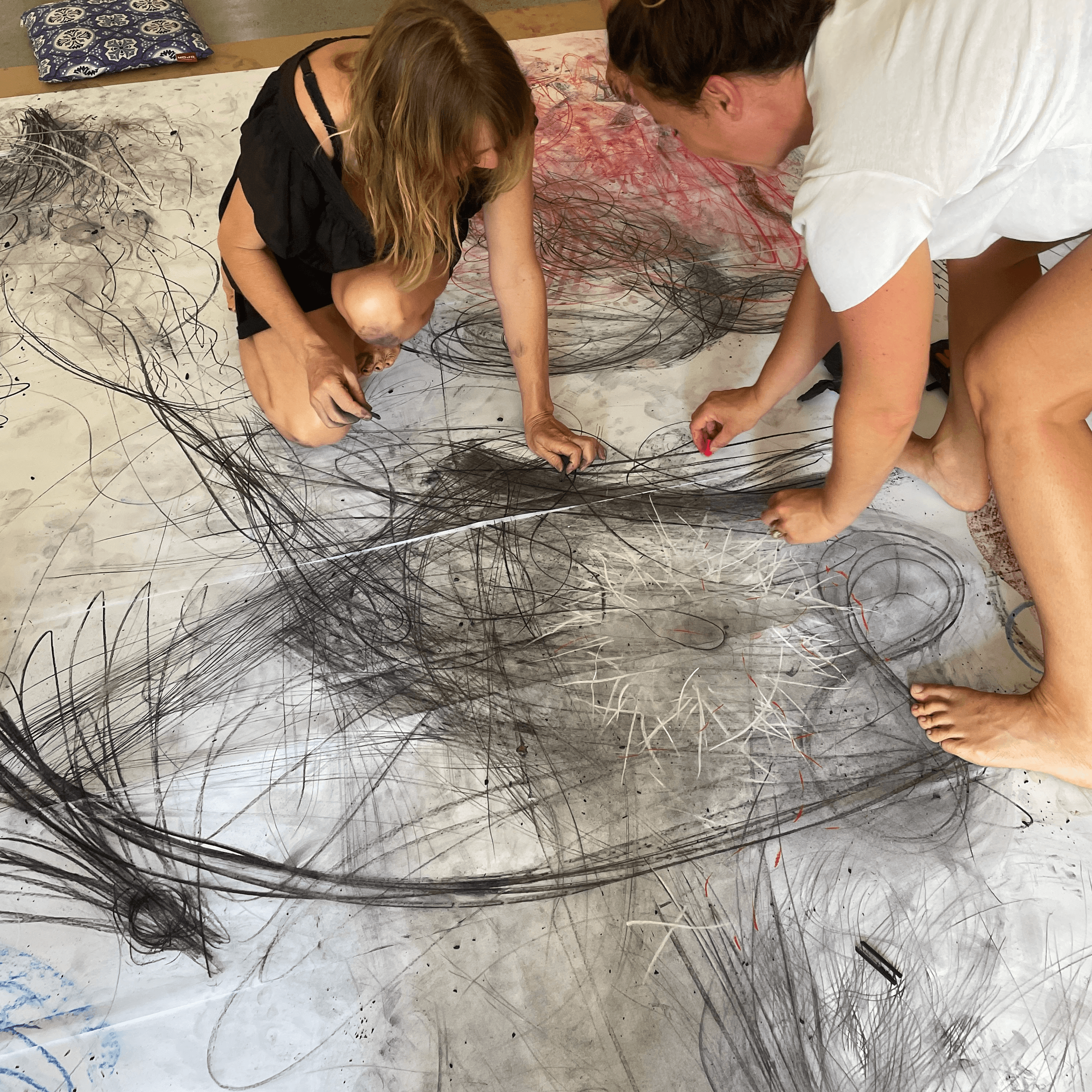 Artists kneeling around a large sheet of paper, drawing together in charcoal