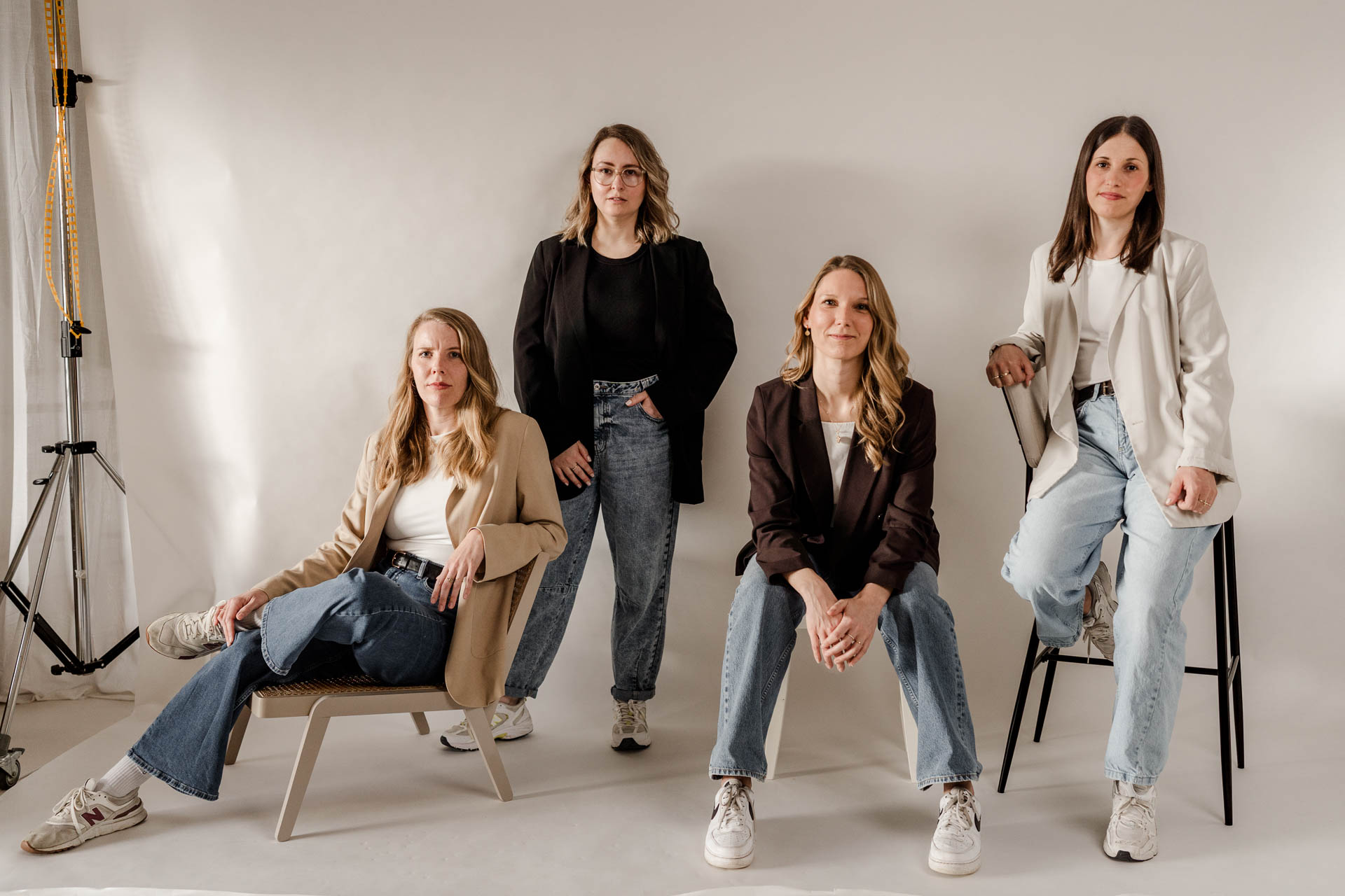 Das engagierte Team-Foto von OHNORD studio aus Straubing vor einer hellen Studiowand. Vier Kolleginnen präsentieren sich selbstbewusst und ausdrucksstark in verschiedenen Posen. Sie tragen moderne minimaoistische Business-Casual-Kleidung, darunter Blazer und Jeans. Der moderne, professionelle Look steht für unsere Arbeitsweise im website studio.