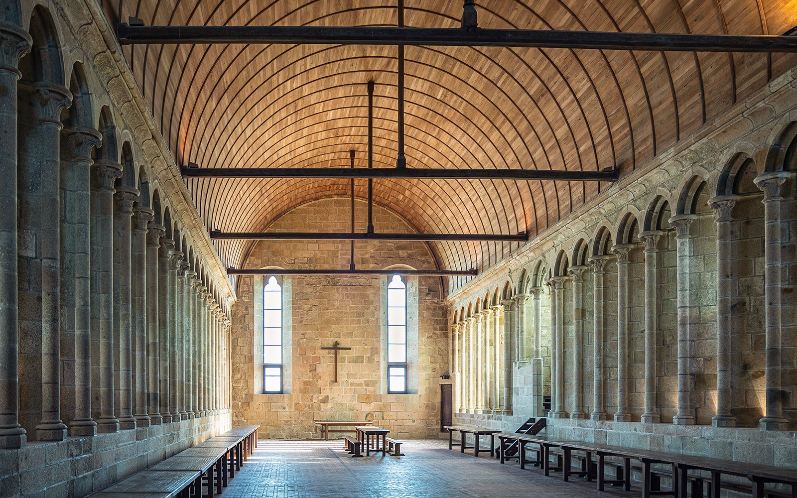 Interior of Mont St. Michel abbey with arched stone columns and wooden ceiling.