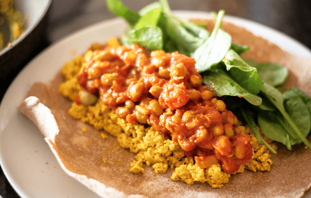 A wholegrain flatbread with golden turmeric scrambled tofu, fresh spinach and chickpea baked beans