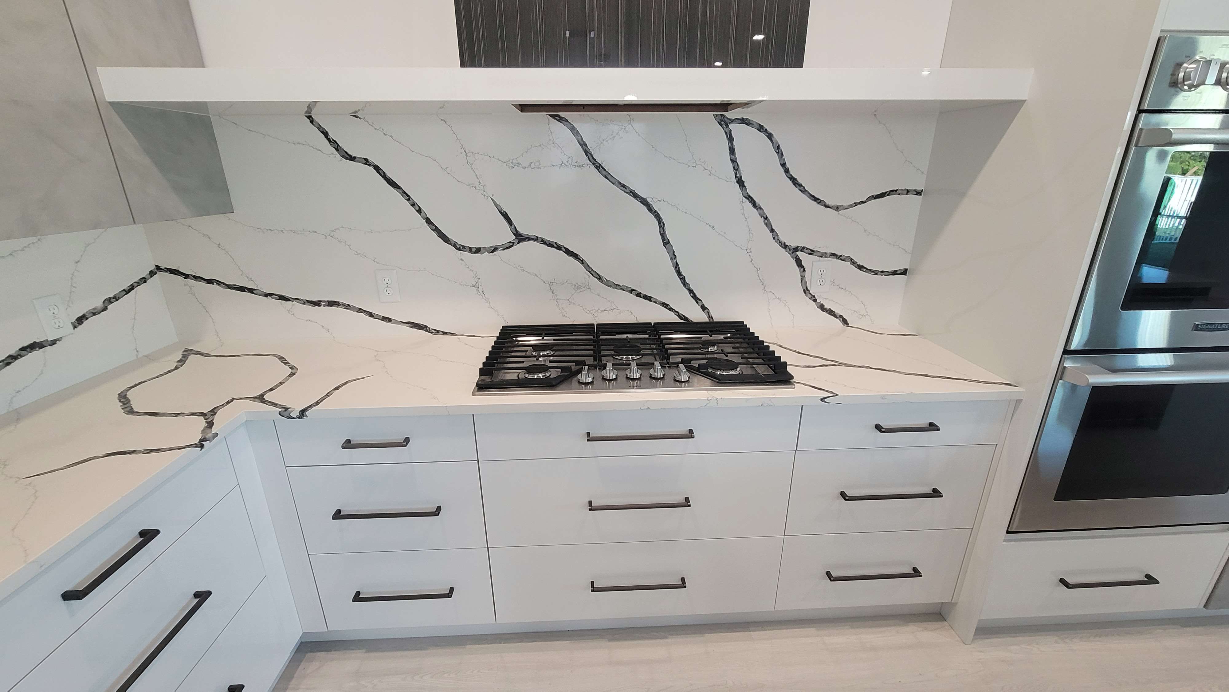 High gloss white base cabinets, with ash gray handles, calacatta laza night countertop and backsplash, and  integrated hood hidden behind Lioher Euroline 3 panels