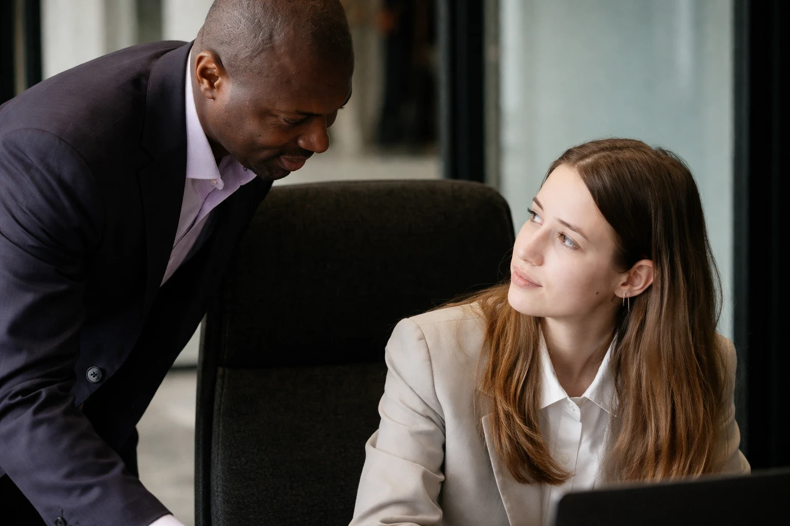 Man in suit leans towards woman at desk.