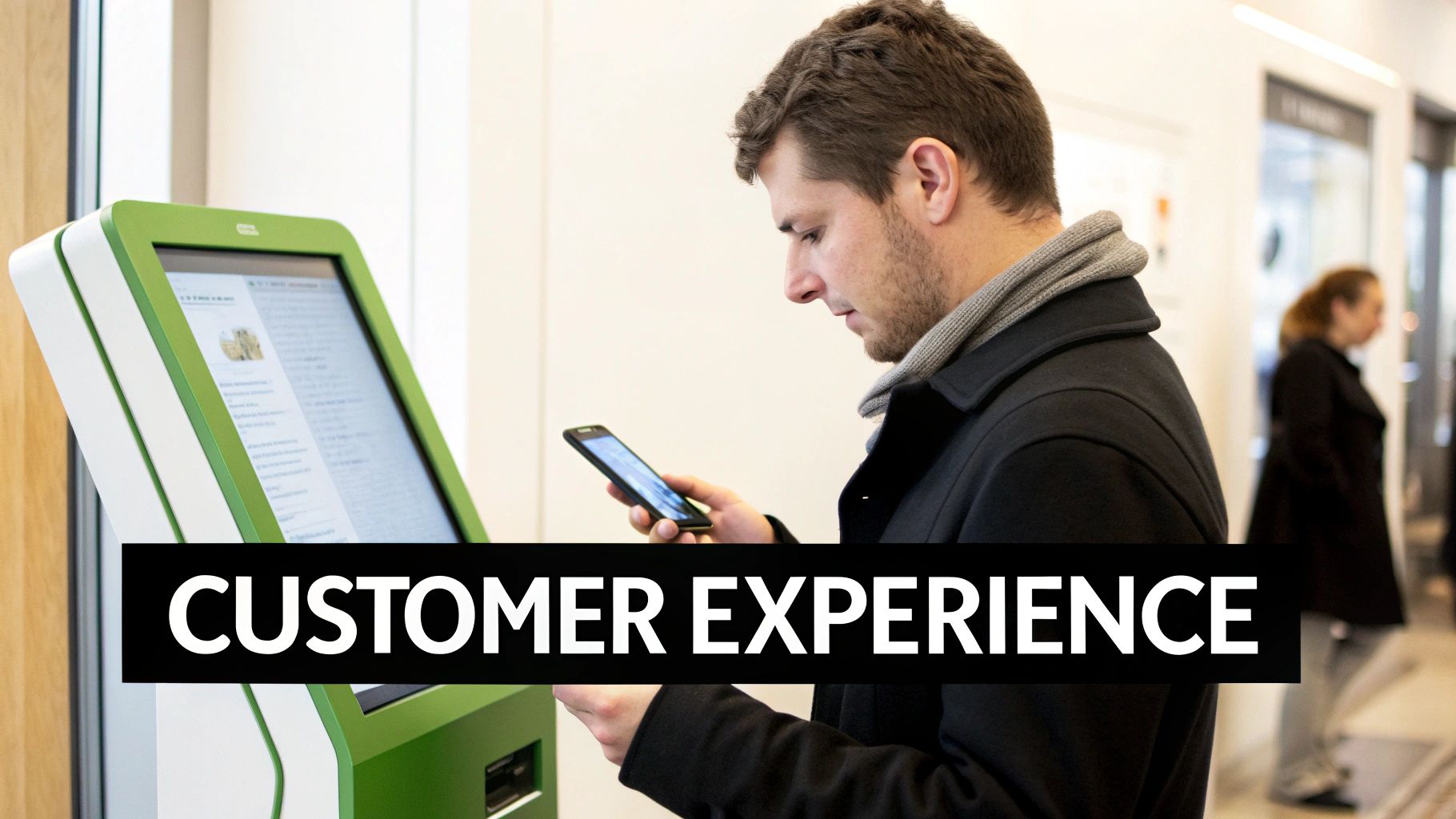 A man uses his smartphone while standing next to a green digital self-service kiosk.