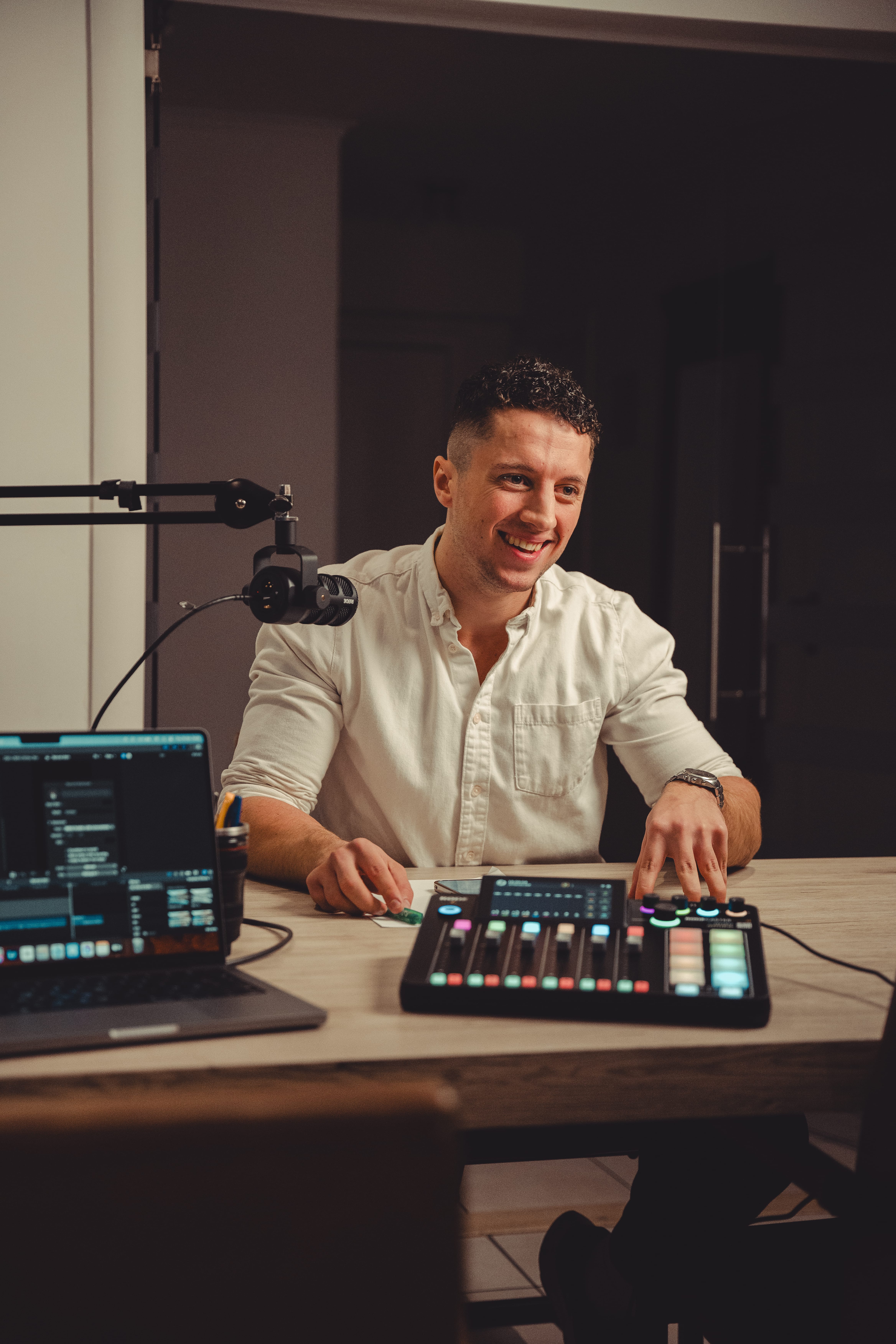 Samuel David van SDSportsPerformance kijkt lachend naar de interviewer terwijl hij op een stoel zit in een podcast-setting, tijdens een interview, met een opvallende microfoon in beeld.